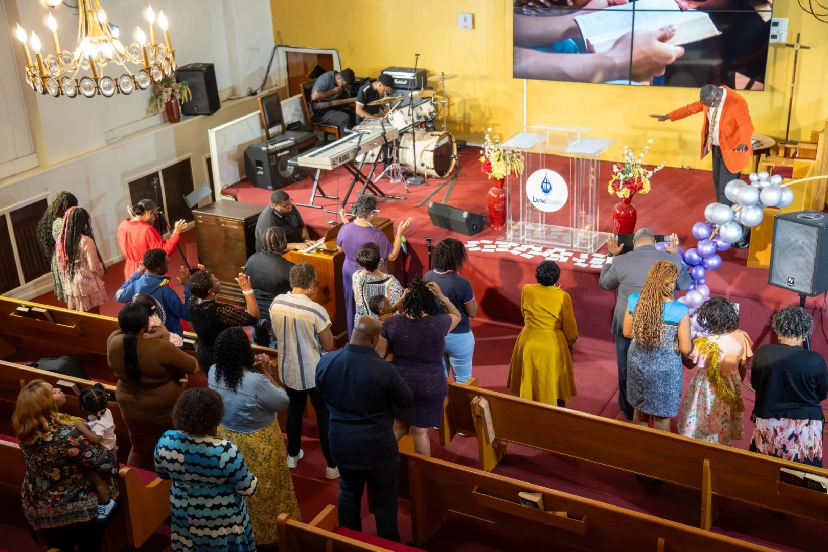 church_audience A congregation stands and prays in a church with a pastor at the front, near musical instruments and a screen.