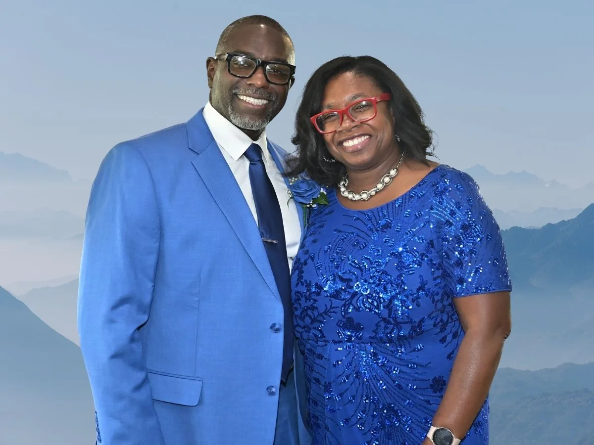 pastors 4 A smiling couple in matching blue outfits, standing against a misty mountain backdrop.
